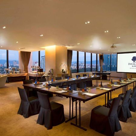 Doubletree By Hilton Kuala Lumpur Hotel Kültér fotó The photo shows a modern conference room. It features a long table arranged for a meeting, with black chairs and notepads placed at each seat. The room has large windows that let in natural light and offer a view of the city outside. On one wall, the