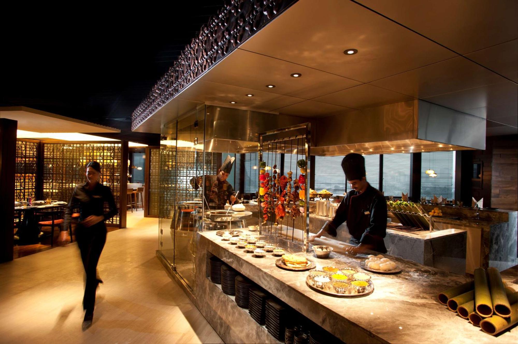 Doubletree By Hilton Kuala Lumpur Hotel Kültér fotó The photo depicts a modern restaurant interior with a sleek and sophisticated design. In the foreground, there is a chef working at an open kitchen area, preparing food. The kitchen features a glass display that showcases a variety of dishes, along w
