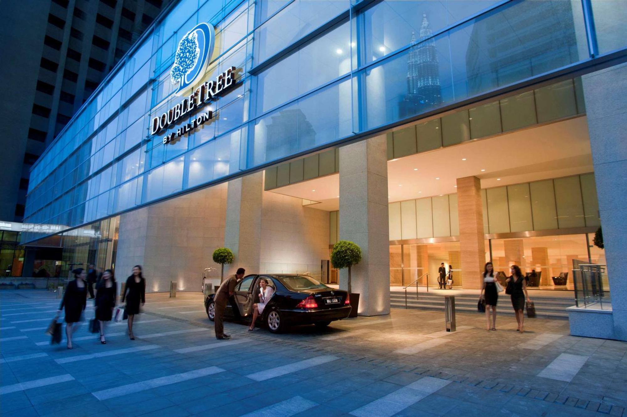 Doubletree By Hilton Kuala Lumpur Hotel Kültér fotó The photo shows the exterior of a DoubleTree hotel. The building features a modern glass facade with the hotel’s logo prominently displayed. In front of the entrance, there is a black car parked, and a few people can be seen, possibly arriving or lea