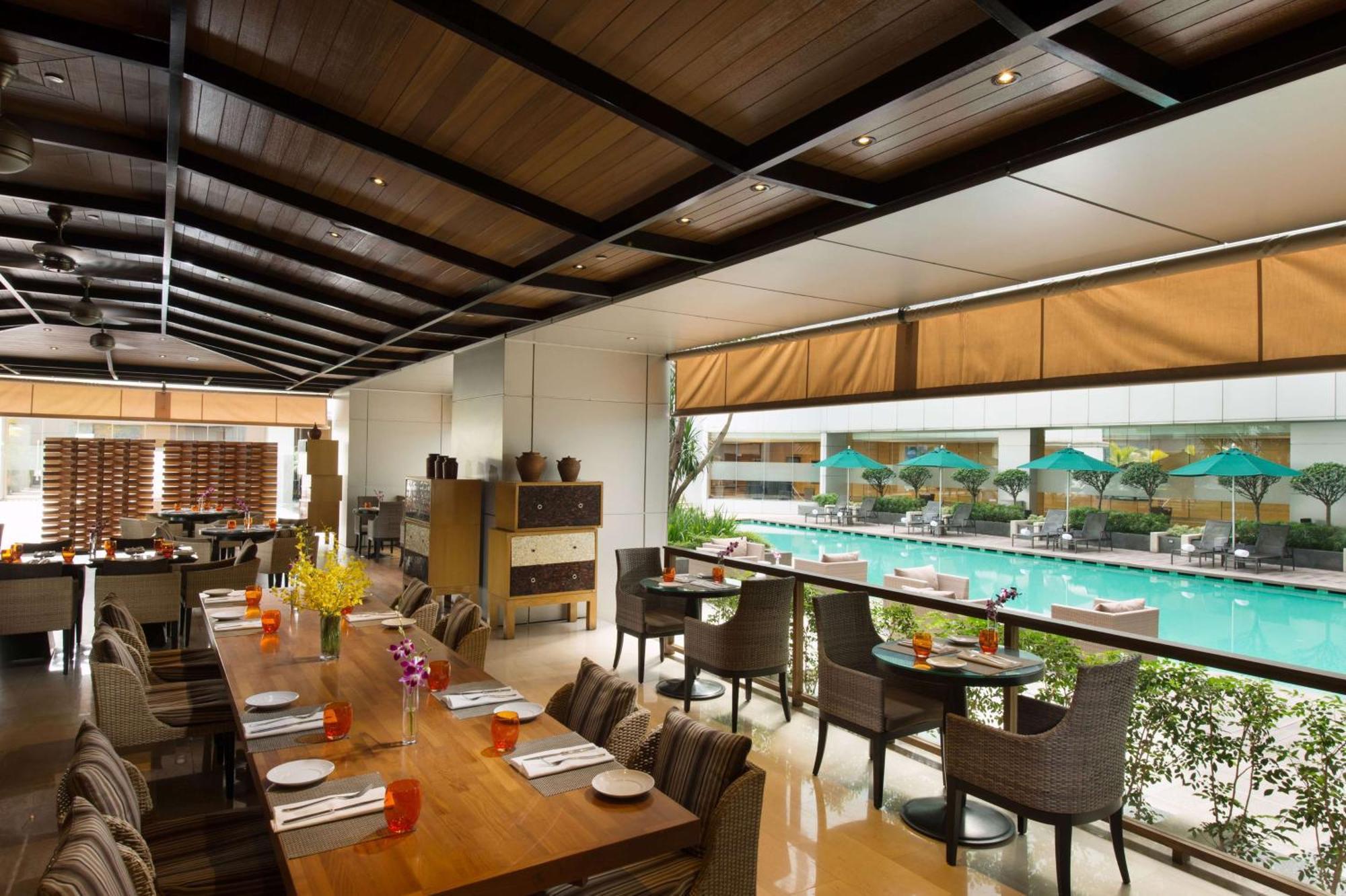 Doubletree By Hilton Kuala Lumpur Hotel Kültér fotó The photo shows an indoor restaurant area with a modern and stylish design. There are several tables set for dining, featuring place settings and drinks. Large windows allow for a view of a swimming pool outside, which is adorned with umbrellas. The 