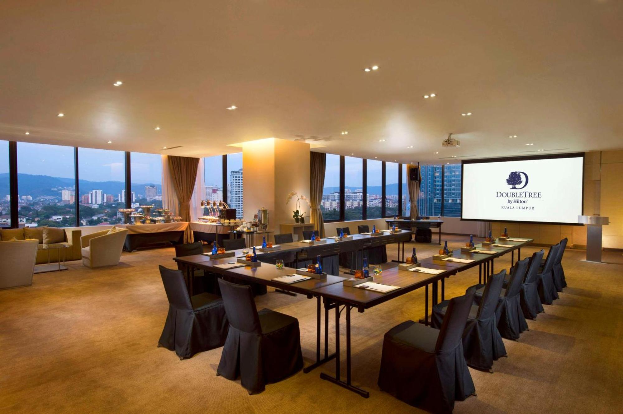 Doubletree By Hilton Kuala Lumpur Hotel Kültér fotó The photo shows a modern conference room. It features a long table arranged for a meeting, with black chairs and notepads placed at each seat. The room has large windows that let in natural light and offer a view of the city outside. On one wall, the