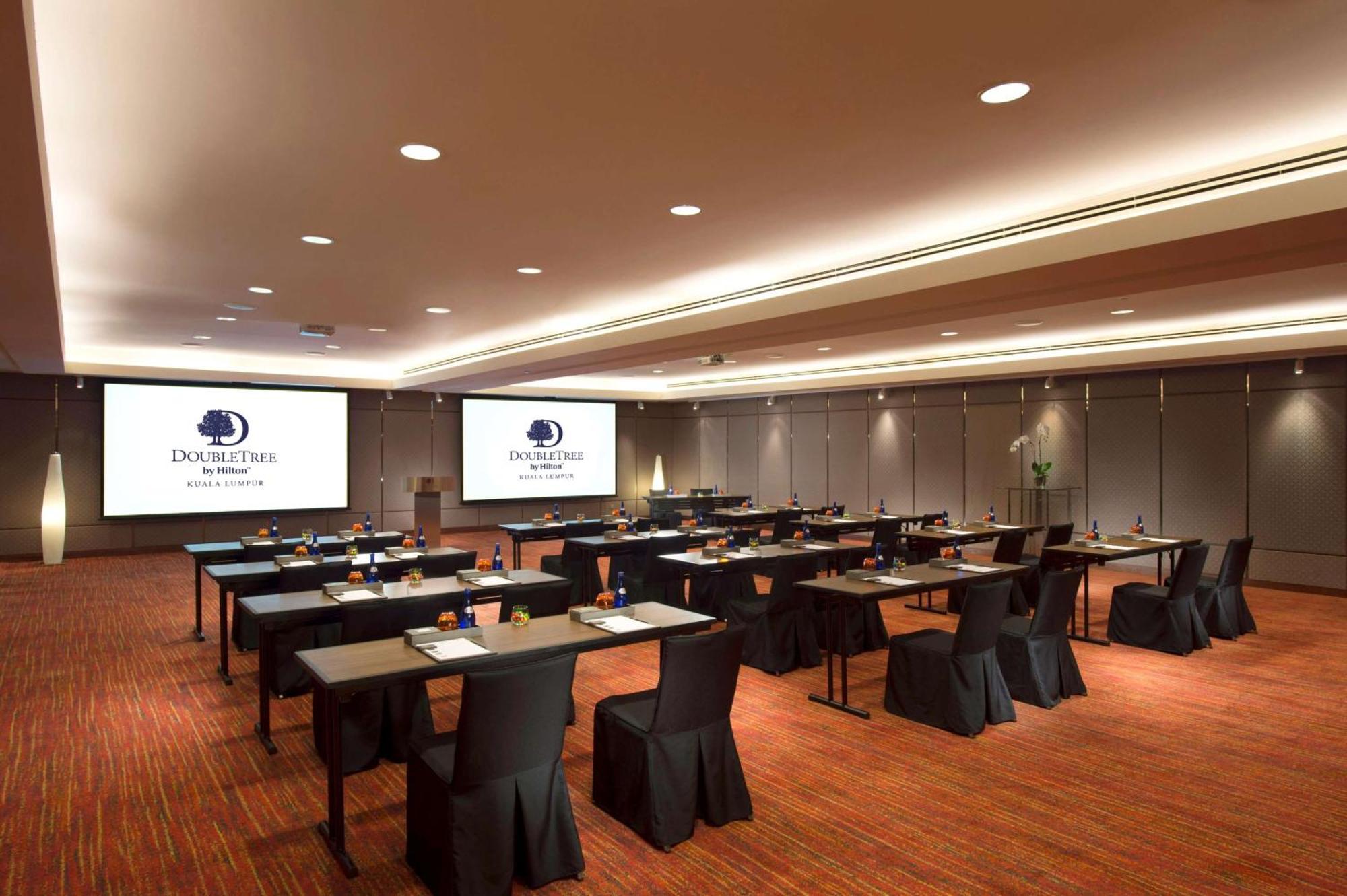 Doubletree By Hilton Kuala Lumpur Hotel Kültér fotó The image shows a conference or meeting room setup. There are several rows of tables arranged for participants, each covered with a black tablecloth. The tables are equipped with stationery, suggesting that the space is intended for a professional ga