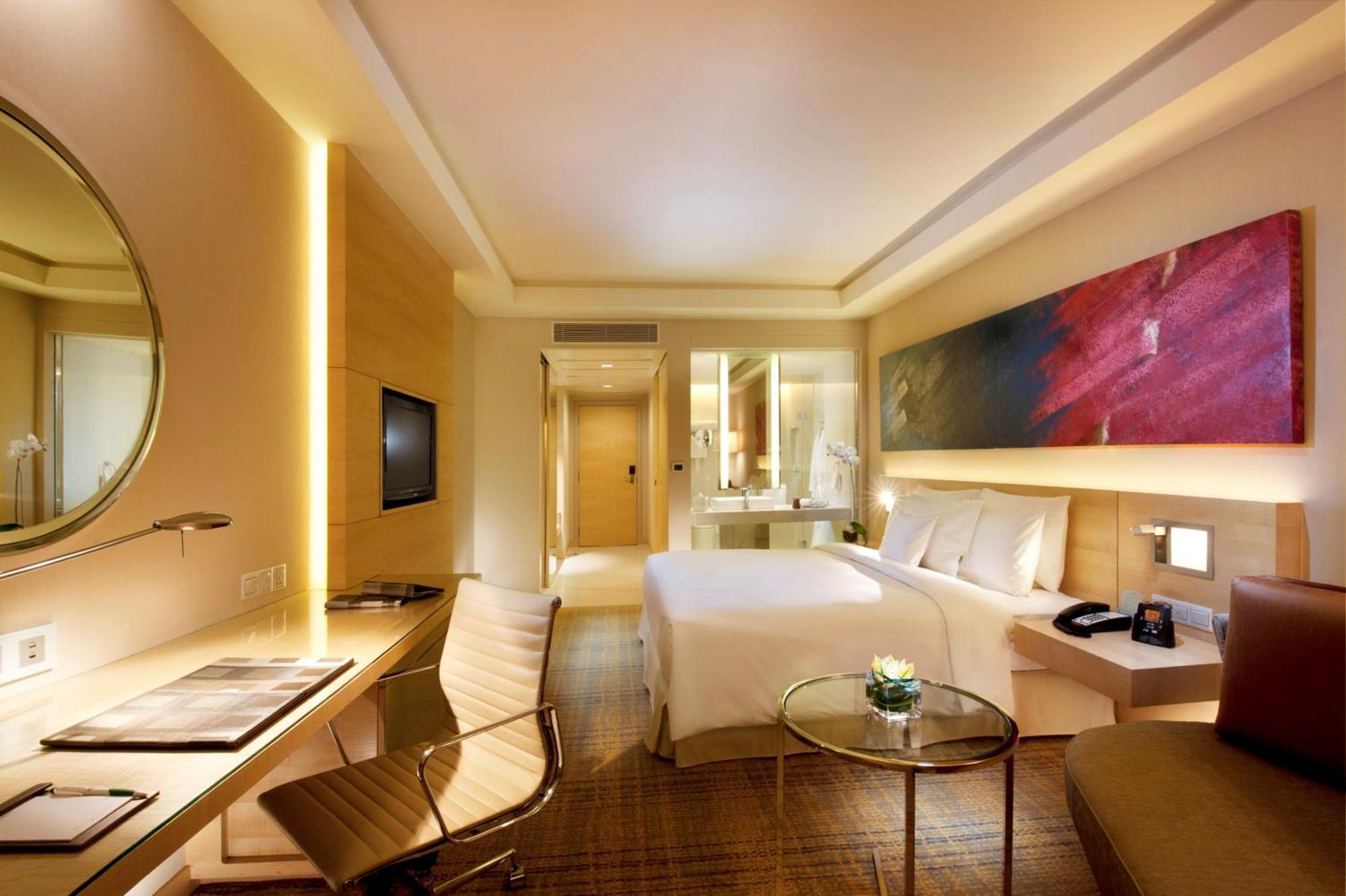 Doubletree By Hilton Kuala Lumpur Hotel Kültér fotó The image shows a modern hotel room featuring a large bed with white bedding, a stylish desk with a chair, and a circular mirror above the desk. There is a flat-screen TV mounted on the wall and a colorful artwork above the bed. The room is well-lit 